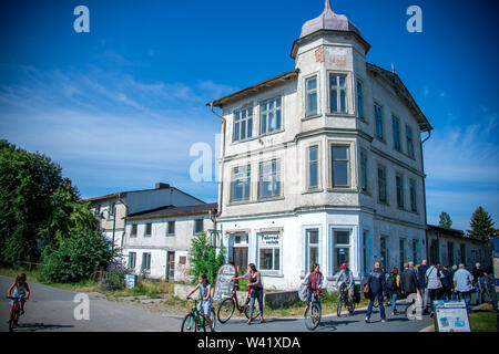11 July 2019, Mecklenburg-Western Pomerania, Kloster: Holidaymakers pass an empty house in Vitte on the Baltic island of Hiddensee. The writer Gerhart Hauptmann stayed in the building from 1896 to 1899. Thousands of holidaymakers and day guests are counted daily on the island during the summer months. Hiddensee is largely car-free and horse and cart is a widely used means of transport. Hiddensee is about 16.8 kilometres long, at its narrowest point about 250 metres wide and at its widest about 3.7 kilometres wide. Within the National Park Vorpommersche Boddenlandschaft it is the largest island Stock Photo