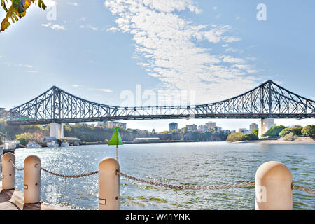 River waterside and concrete pillar fence with a long and metal bridge under the blue sky with clouds Stock Photo