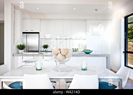 Dining table with candle beside a fancy thread ball on the white surface in the kitchen with green plants on the counter next to fridge hanging lights Stock Photo