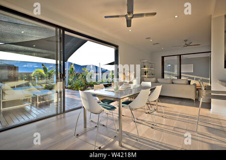 Dinner on the wooden floor with a glass door entrance beside chairs and tables near the sofa under the fans, the opened glass panel shows the outside Stock Photo