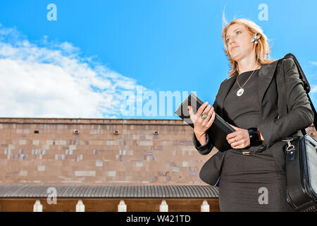 Businesswomen with a black dress looking forward and holing file and documents in front of a building and under blue sky Stock Photo