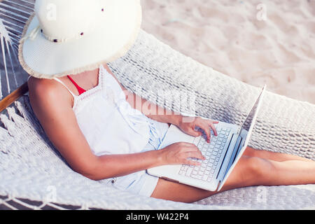 Woman using her laptop in hammock on the beach Stock Photo