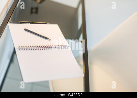 Tilted view of a notebook, pencil and a pen kept on a glass table with a wrought iron frame Stock Photo