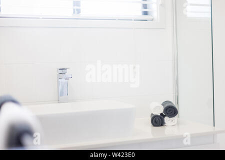 View of a wash basin fitted with a stylish faucet and four rolled up hand towels in black and white kept on the side counter Stock Photo