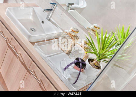 High angle view  of the silver steel tap and white sink with a mirror  on the wall beside a fancy plant in the vase near a towel Stock Photo