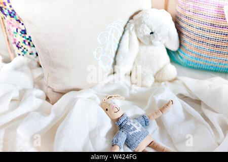 Hare toy dolls on a bed with pillows closeup including small rabbit with dress and a white wool rabbit laying to a pillow Stock Photo