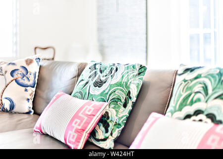 Modern sofa and pillows close up in a room of a modern house, there are green and pink designs on the pillows on the grey leather surface with white w Stock Photo