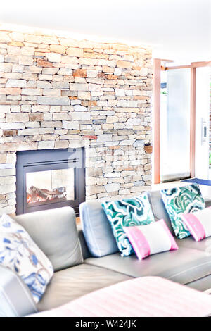 Modern fireplace at home living room with stone walls, there is a door to outside, sofas and pillows blurred Stock Photo
