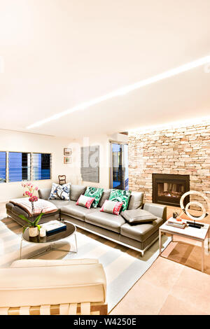 Living room with pillows and leather sofas under bright lights in a modern house, the stone wall and fireplace can be seen behind the chairs and door Stock Photo