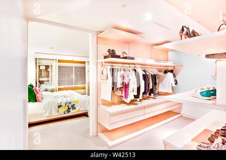 Bedroom attached to the garment store room of a house with ladies and gents shirts  hanging under the racks and shoes on the shelves beside the bedroo Stock Photo