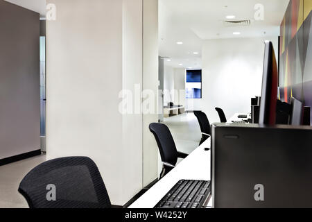Work place with computers, monitors and chairs with a room inside illuminated using lights Stock Photo