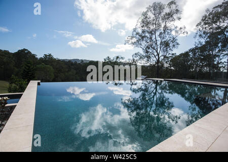 Modern swimming pool, close up from the corner which surrounded by trees in the forest under blue sky with white clouds, the pool is deep and the refl Stock Photo