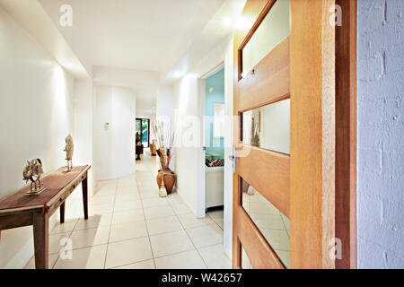 Wooden table and door near home entrance, comfortable furnitures with designs, walls are white color, pillows on chairs, inside rooms of a apartment. Stock Photo