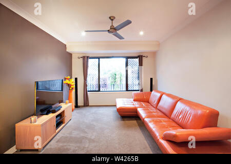 Red sofa near television and table, comfortable furnitures with designs, walls are white color, pillows on chairs, inside rooms of a apartment. Stock Photo