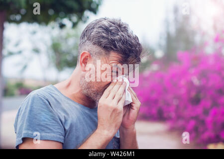 Man sneezing in a tissue outdoors. Pollen allergy, Springtime. Stock Photo