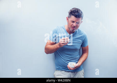 Handsome young man with brown hair wearing shirt isolated on grey background. Smoking cigarette. Stock Photo