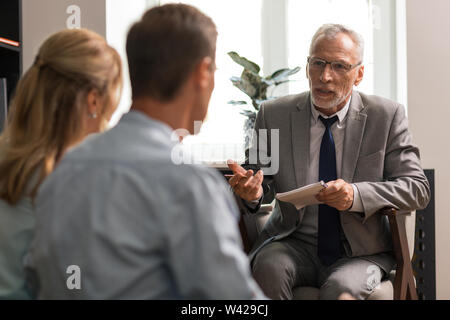 Grey-haired Caucasian senior psychologist talking to a couple Stock Photo