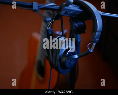 Black studio headphones on a stand and black guitar background. Stock Photo
