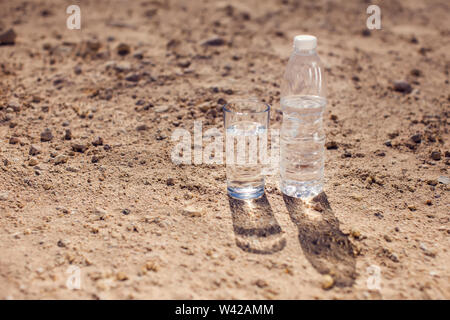 Glass and bottle of water on sand in the desert. Thirsty, heat and drought concept Stock Photo
