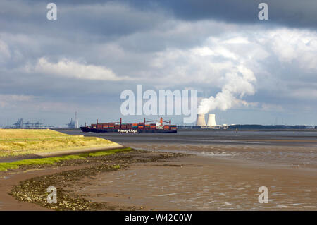 A container ship sailing over the Western Scheldt at low tide with the Doel nuclear power plant cooling towers in the background on Walcheren in Zeela Stock Photo