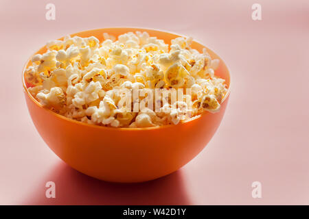 An orange bowl with popcorn isolated on pink background. Food concept Stock Photo