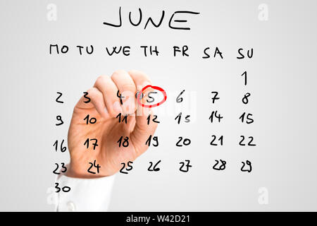 Close up of the hand of a man marking off World Environment Day, the 5th of June, on a hand-written calendar on a virtual screen ringing it with a red Stock Photo