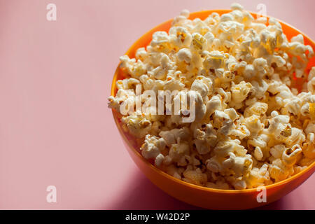 An orange bowl with popcorn isolated on pink background. Food concept Stock Photo