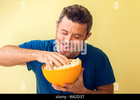 Portrait of a funny man eating popcorn over yellow background Stock Photo