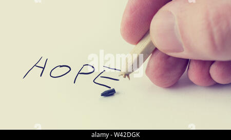 Retro image of a man writing the word Hope on notepaper with a pencil on which the graphite point has just broken with the broken piece lying alongsid Stock Photo