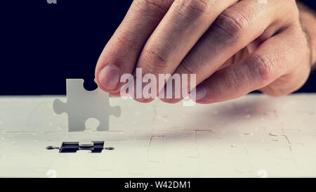 Close up of the hand of a man placing the last piece in place in a jigsaw puzzle conceptual of problem solving, finding a solution and meeting a chall Stock Photo
