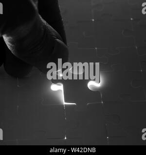 Man completing a jigsaw puzzle placing the last piece in position over the remaining gap with light streaming through in a concept of problem solving, Stock Photo