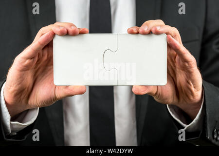 Businessman holding two interlocked blank white jigsaw puzzle pieces in his hand depicting the completion of a deal, solution to a problem or overcomi Stock Photo