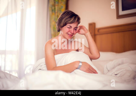 Young sad woman with short hair is lying in her bed and crying. People and lifestyle concept Stock Photo