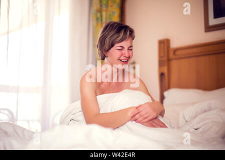 Young sad woman with short hair is lying in her bed and crying. People and lifestyle concept Stock Photo