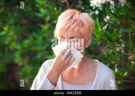 Young woman with short hair sneezing into tissue. flu, allergy, runny nose. People and healthcare concept