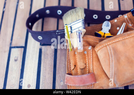 Leather tool belt with construction tooling on wooden board. Maintenance concept. Stock Photo
