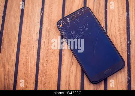 Mobile smartphone with broken screen on wooden background. Stock Photo