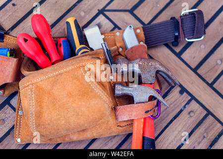 Leather tool belt with construction tooling on wooden board. Maintenance concept. Stock Photo
