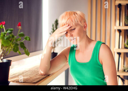 Portrait of young woman with short hair touching her temples feeling stress indoor. People and healthcare concept Stock Photo