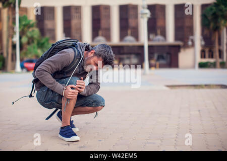 Close up of a man sitting and holding his knee in pain due to injury outdoor. People, health care, medical concept Stock Photo