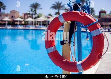 Red emergency lifebuoy hanging on fence near sea or pool Stock Photo