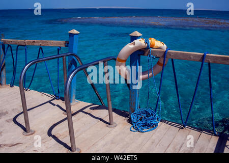 Red emergency lifebuoy hanging on fence near sea or pool Stock Photo