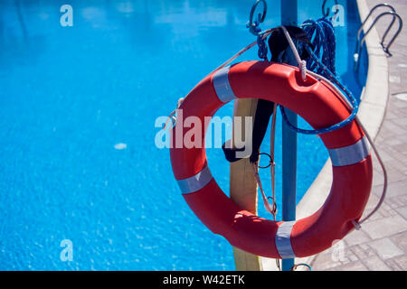 Red emergency lifebuoy hanging on fence near sea or pool Stock Photo