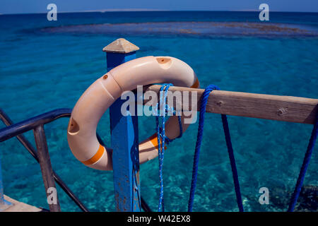 Red emergency lifebuoy hanging on fence near sea or pool Stock Photo