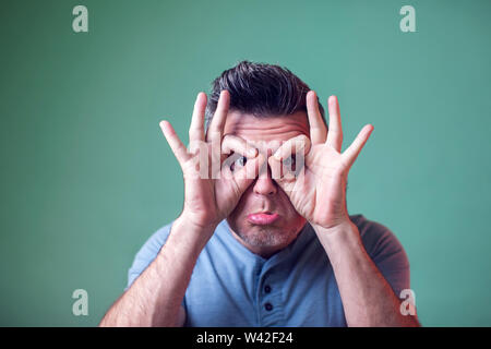 Young man showing owl sign with fingers. Making funny grimace. Have a good mood. People, emotions and lifestyle Stock Photo