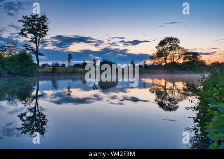 evening view of the water with trees and clouds reflected in the water Stock Photo
