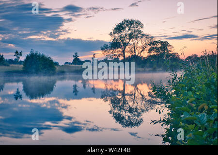 evening image with fog on the water with trees and clouds reflected in the water Stock Photo