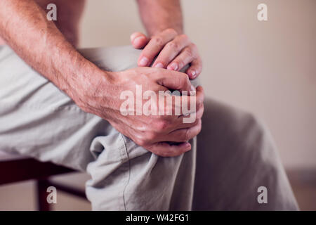 Close up of a man sitting and holding his knee in pain due to injury on white background. Healthcare, medicine and people concept Stock Photo