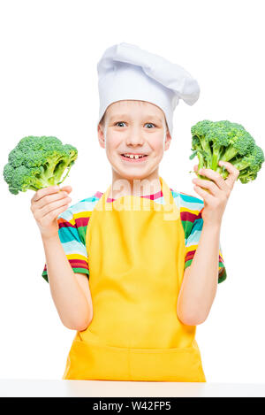 emotional portrait of a boy cook in hat and apron with broccoli on white background isolated Stock Photo