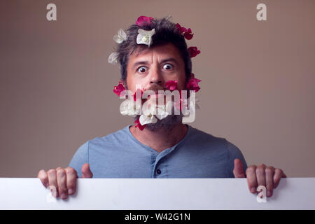 Handsome surprised man with flowers on his beard and hair. People, emotions, summer or spring concept Stock Photo